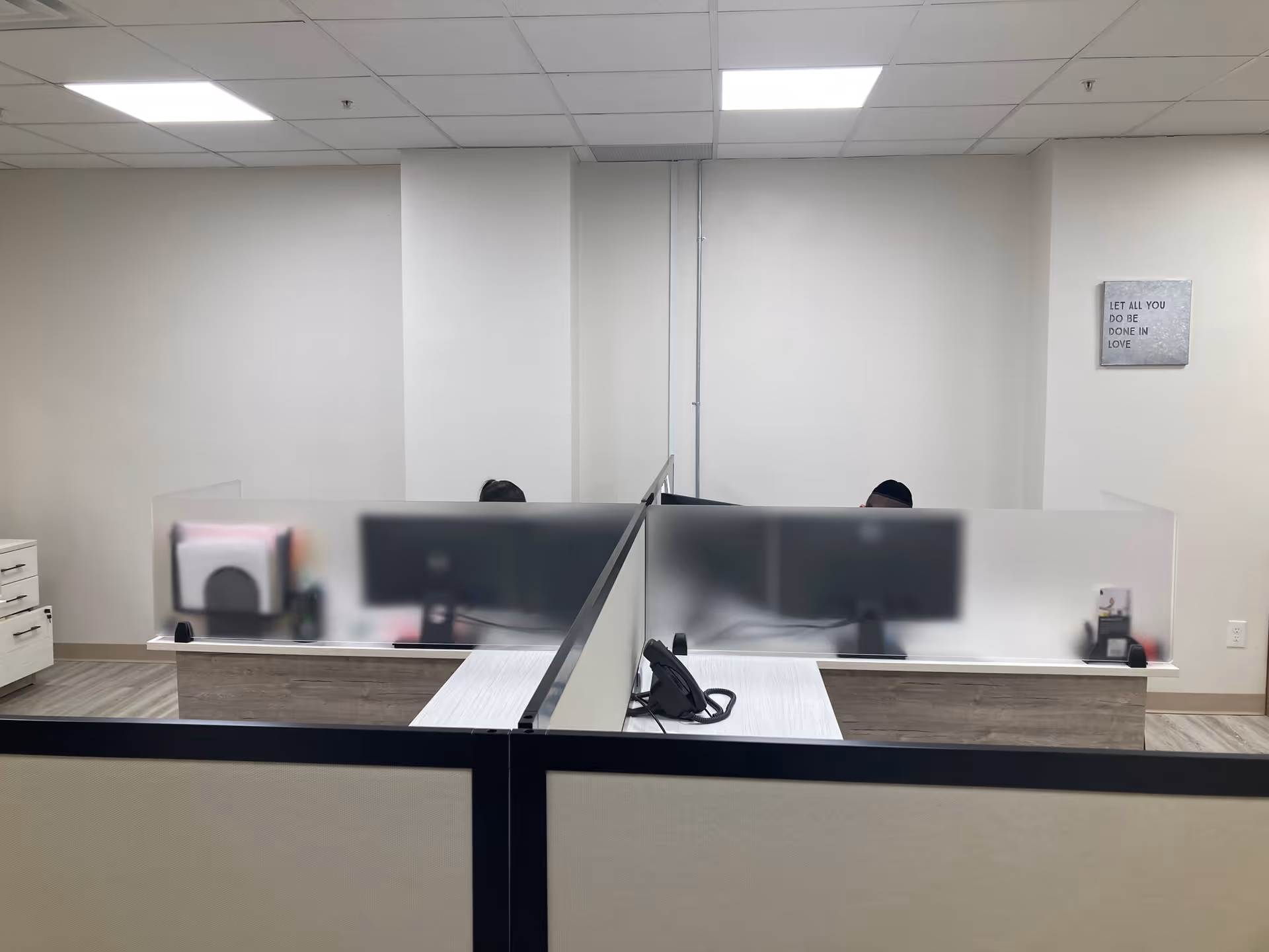 Interior office space with frosted cubicle partitions and two staff desks.