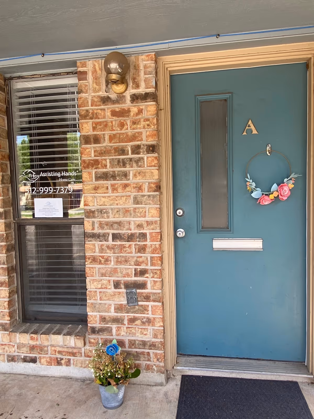 Brick exterior with teal door labeled A, wreath, window, and potted plant.