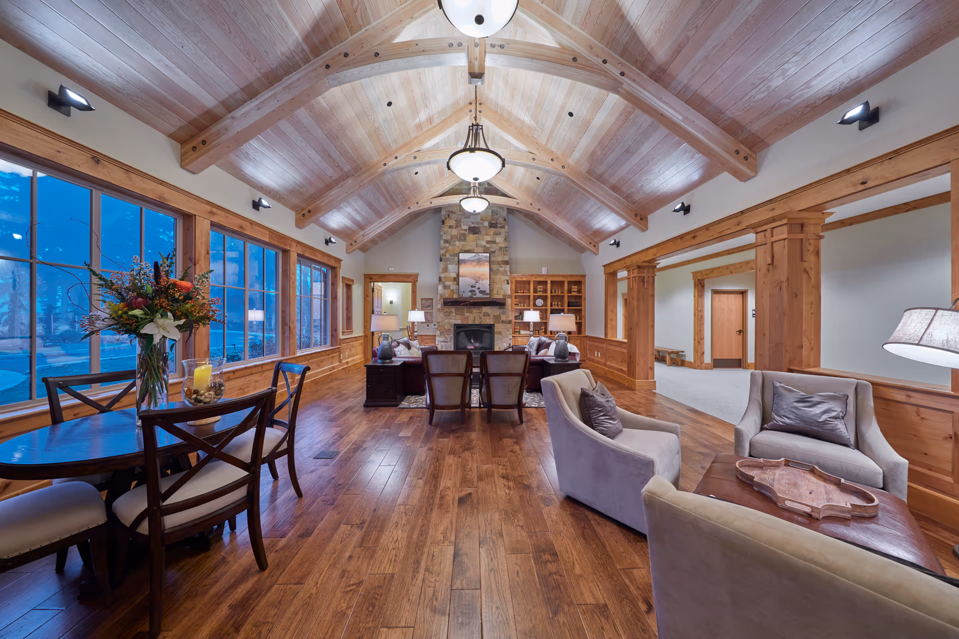 A spacious living room with wooden floors, a stone fireplace, large windows, and comfortable seating.