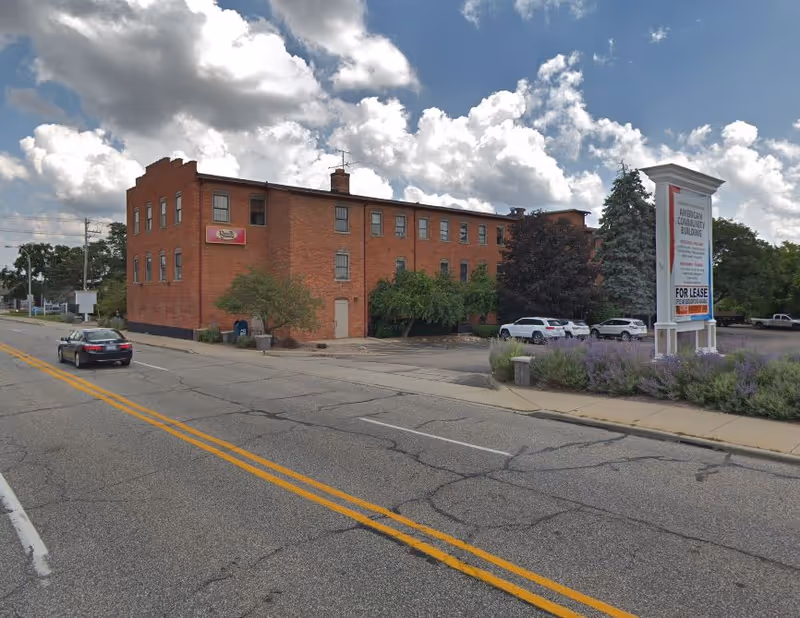 Brick three-story building on a street corner with a large roadside sign.