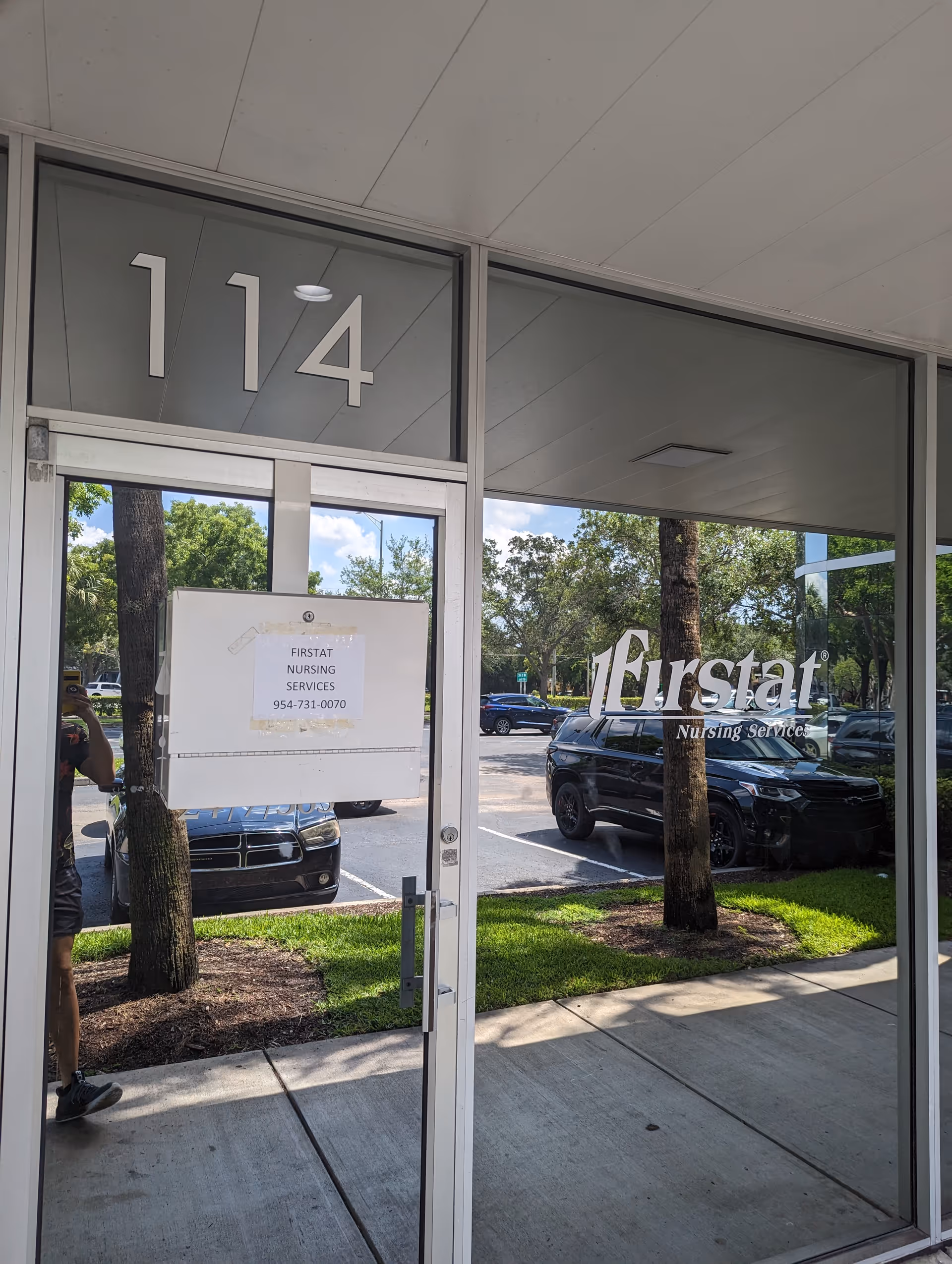Glass front entrance of Firstat Nursing Services with unit number 114 and reflected parking.