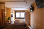 Interior view of a patient room with a bed, window, and wall-mounted TV.