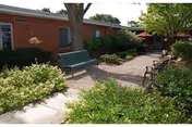 Outdoor courtyard at The Manor of Novi with benches, brick walkway, and greenery.