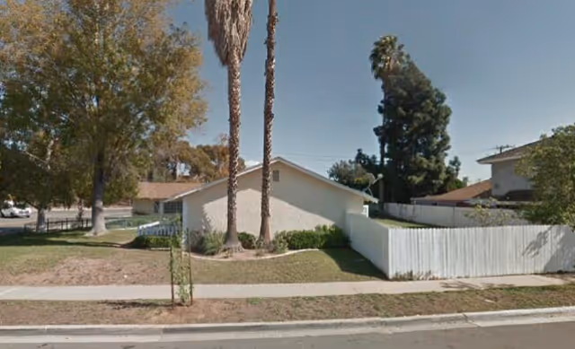 Exterior view of a single-story building with a white fence and palm trees.
