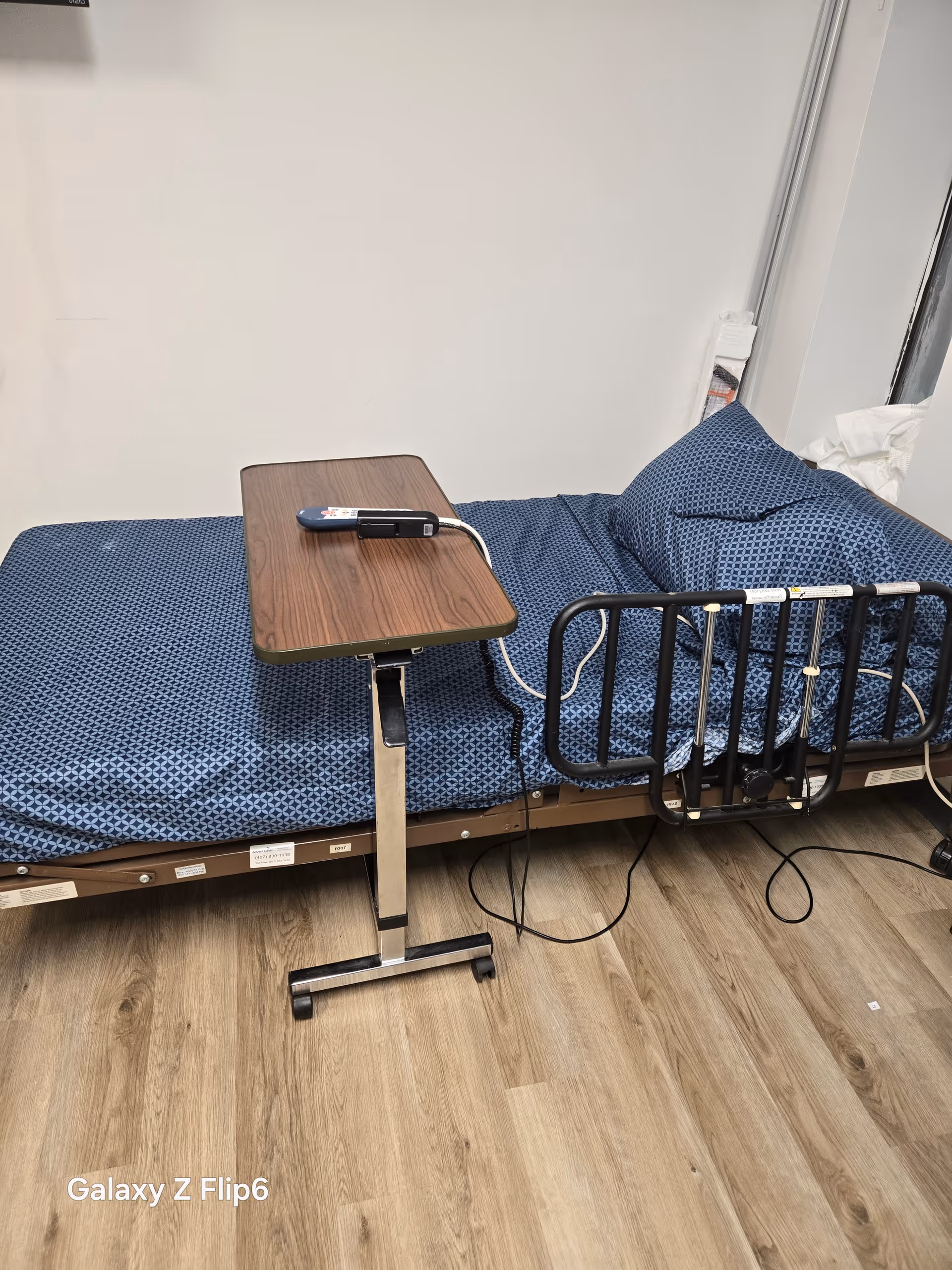 Hospital-style bed with blue patterned sheets and an overbed table in a patient room.