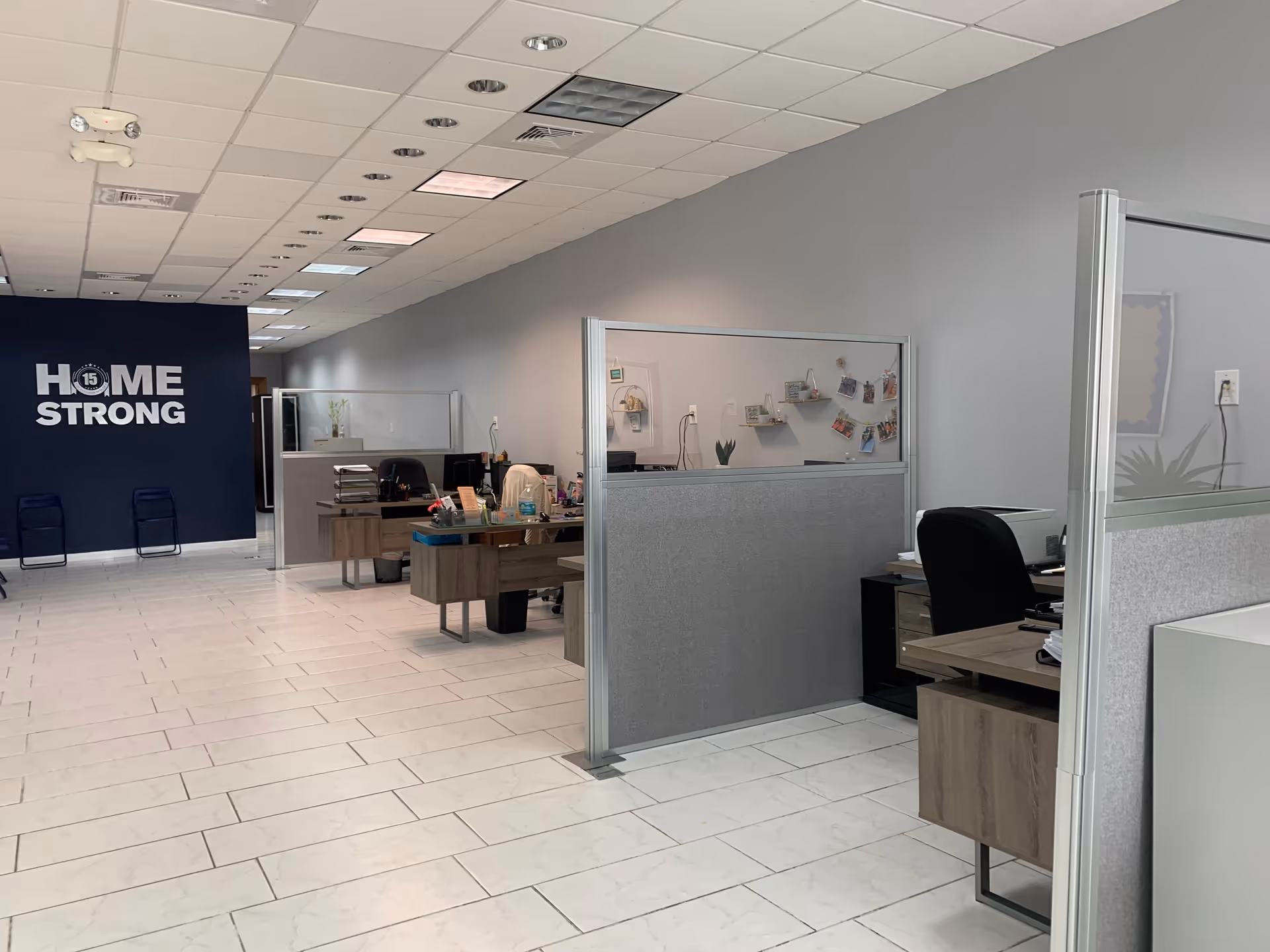 Wide interior office area with cubicles, desks, and a blue wall reading HOME STRONG.