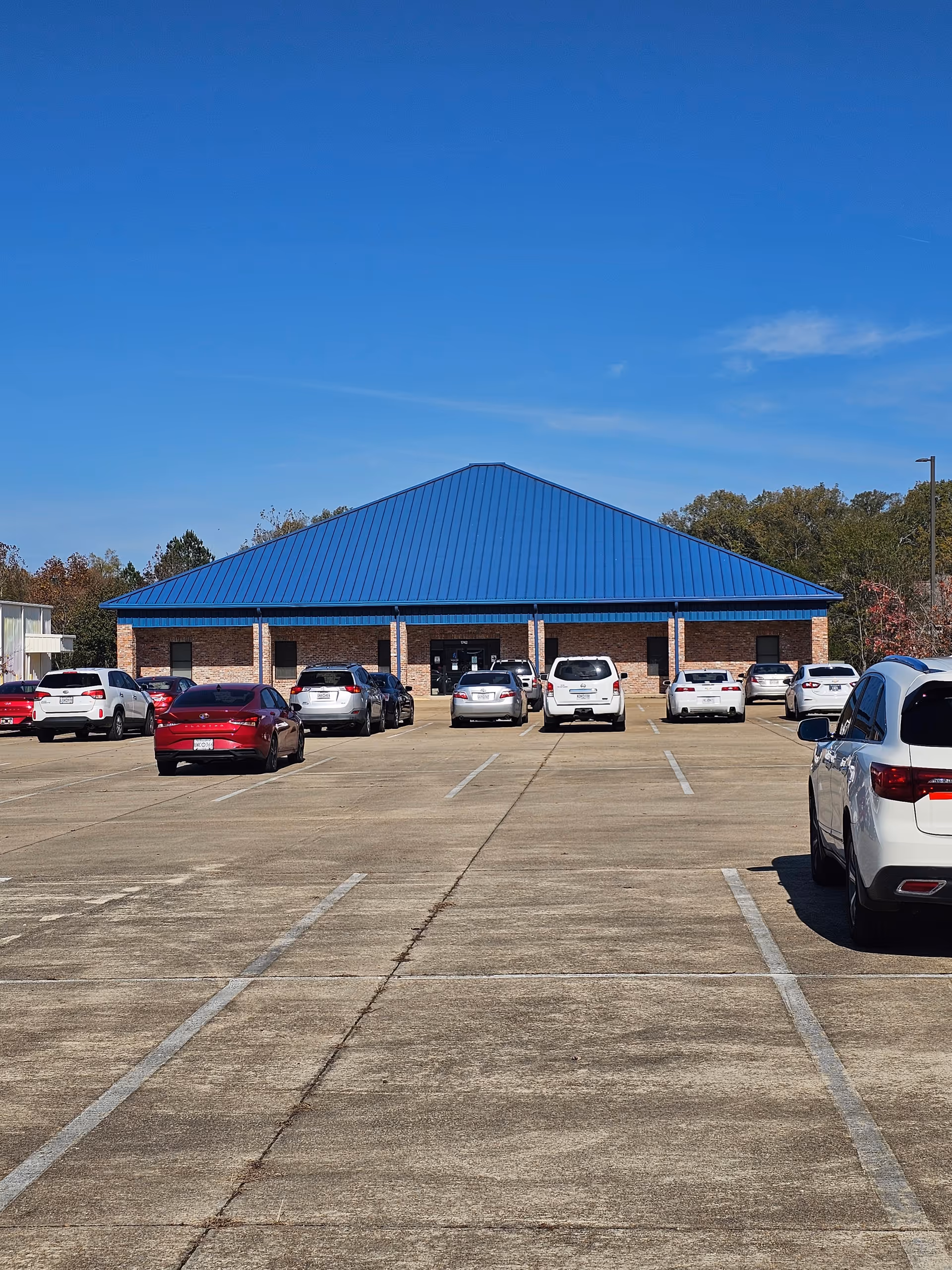 Blue-roofed brick building fronts a spacious parking lot.
