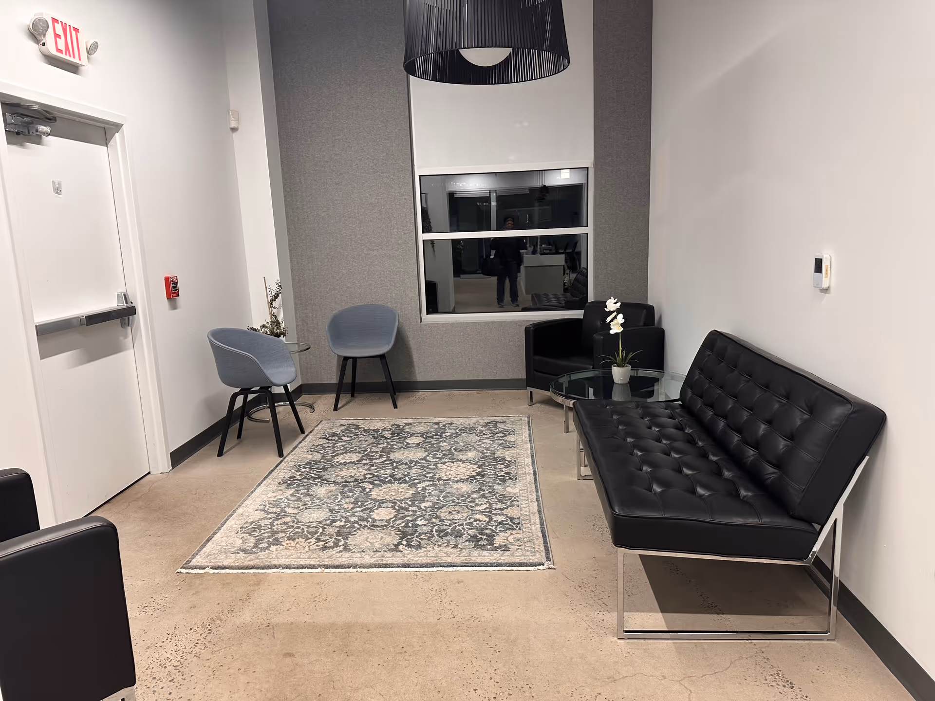 Waiting area in Home Sure Home Care with black leather sofa, chairs, rug, and glass table.