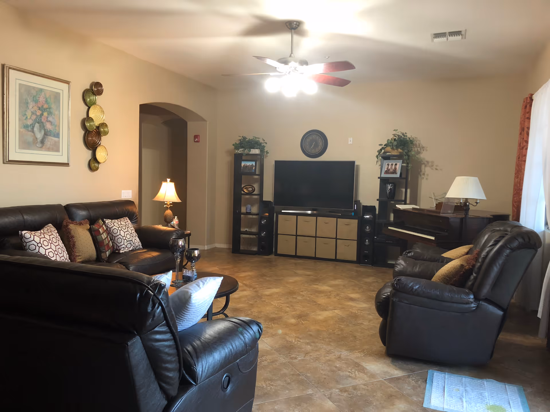 Cozy living room with leather sofas, a TV stand, piano, and warm lighting.