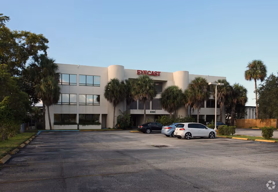 Exterior view of a modern two-story building with palm trees and a parking lot.