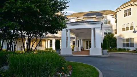 Exterior view of Atria Plainview entrance with white columns and landscaped grounds.