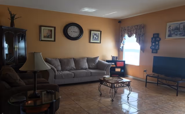 A cozy living room in a senior facility with tan walls, sofa, TV, and coffee table.