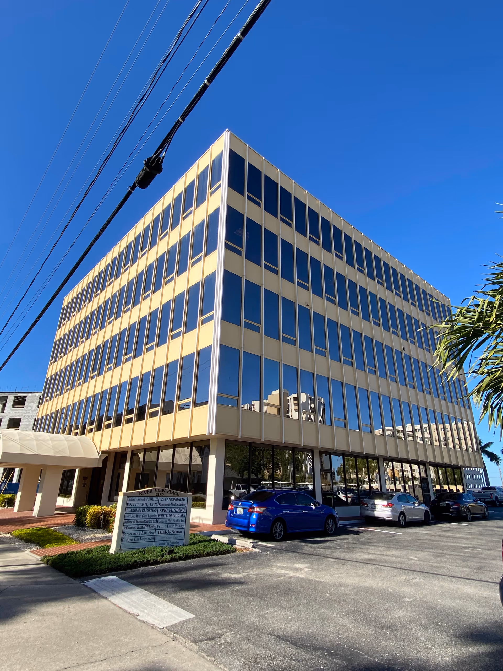 A multi-story beige glass-paneled office building with blue sky and a parking lot.