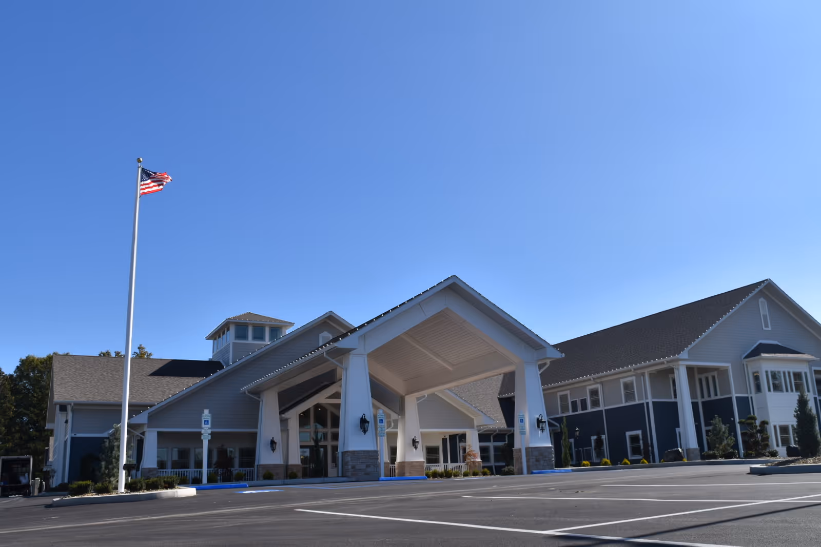 Modern senior living facility with a wide front entrance, flagpole, and blue sky.