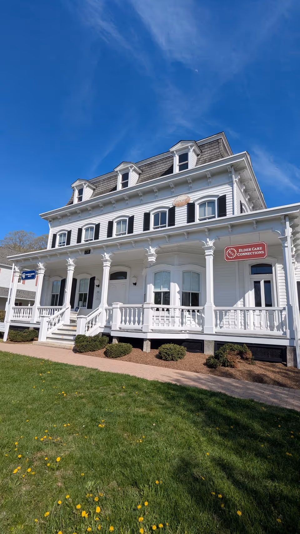 White, two-story elder care building with a wraparound porch and neatly trimmed lawn.