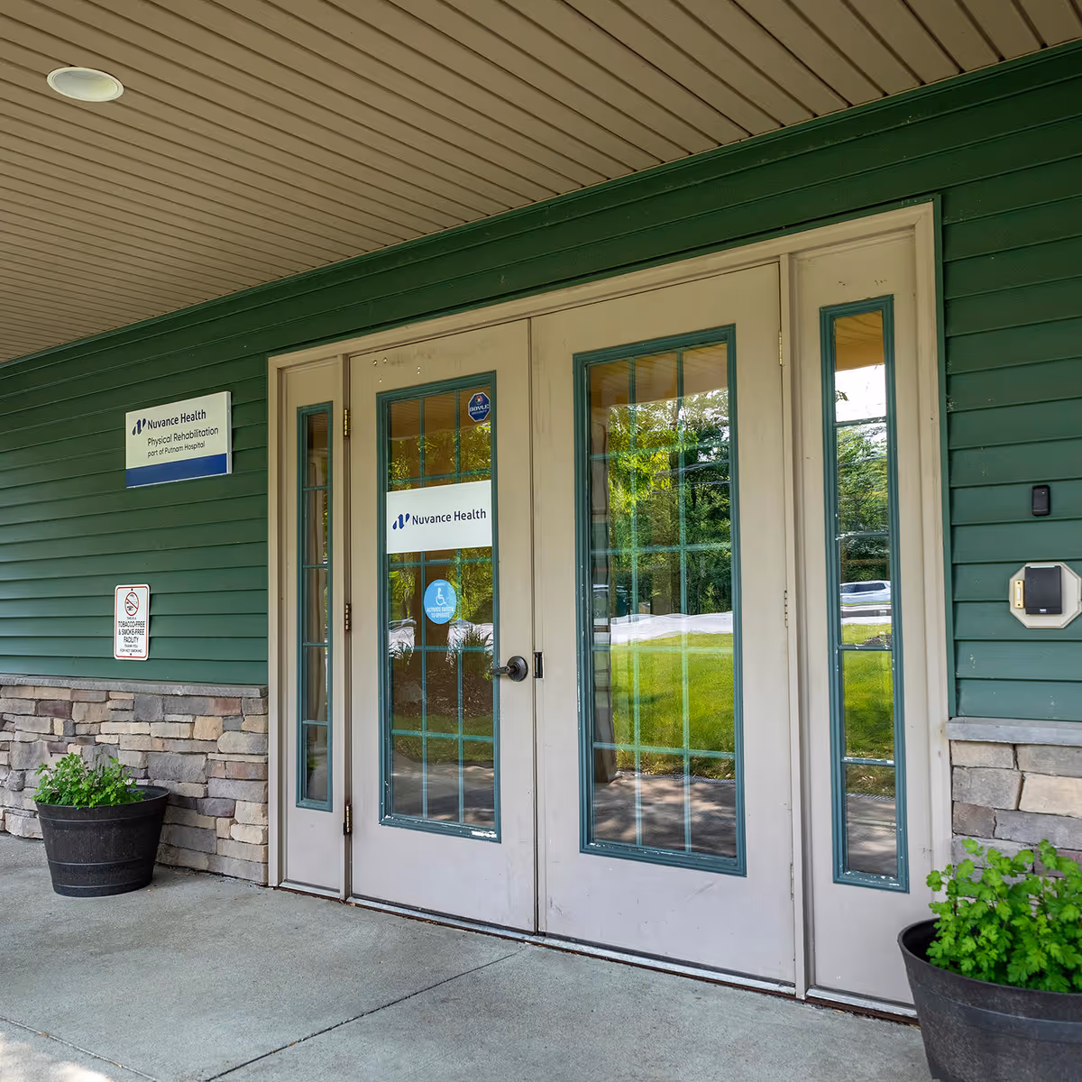Green building exterior with double glass doors and potted plants at the entrance.