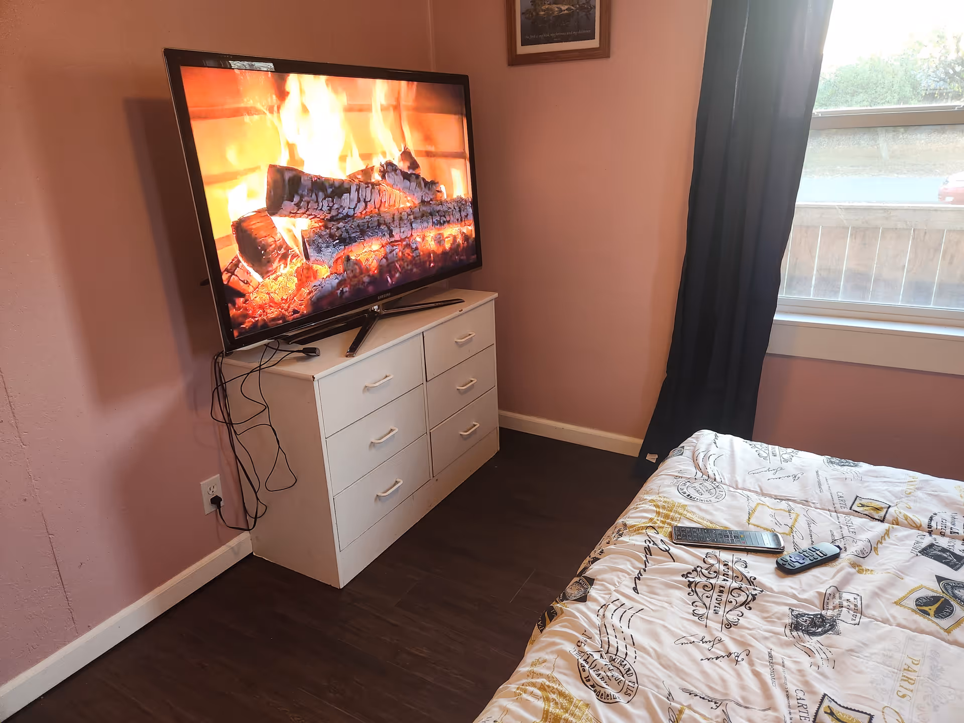 A bedroom with a TV on a white dresser, pink walls, and a bed.