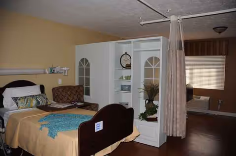 A bedroom in a senior facility with a bed, partition curtain, and shelving.