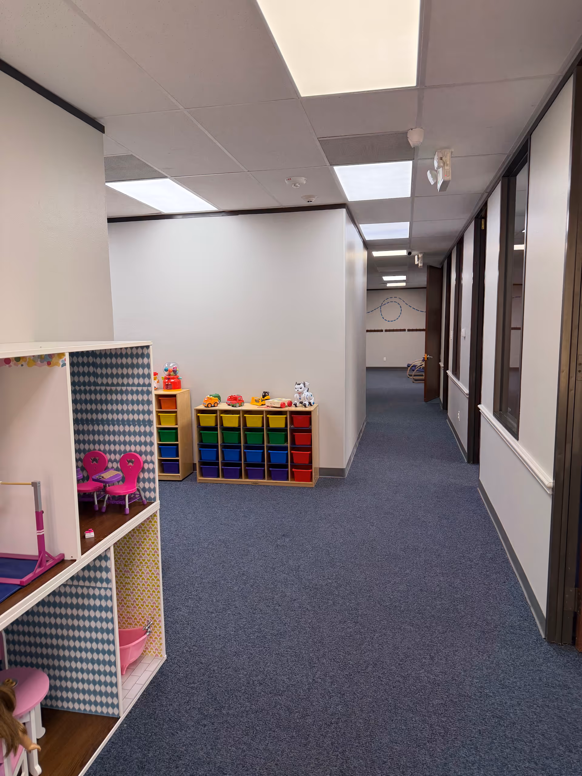 Colorful children's play area with storage cubes along a hallway in a senior living facility.