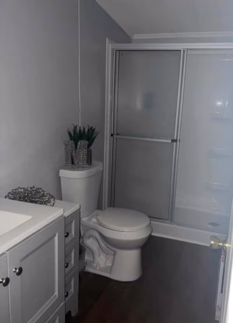 Small gray bathroom with toilet, vanity, and sliding shower door.