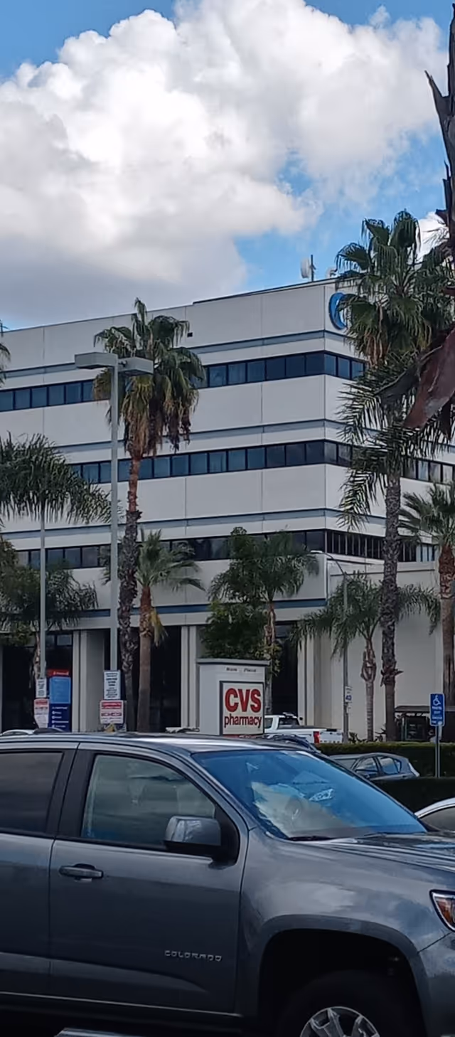 Exterior view of a modern office building with palm trees, parked cars, and a CVS sign.