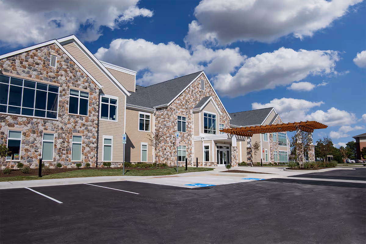 Exterior view of Gilchrist Center Baltimore showing stone façade, parking lot, and wooden pergola.
