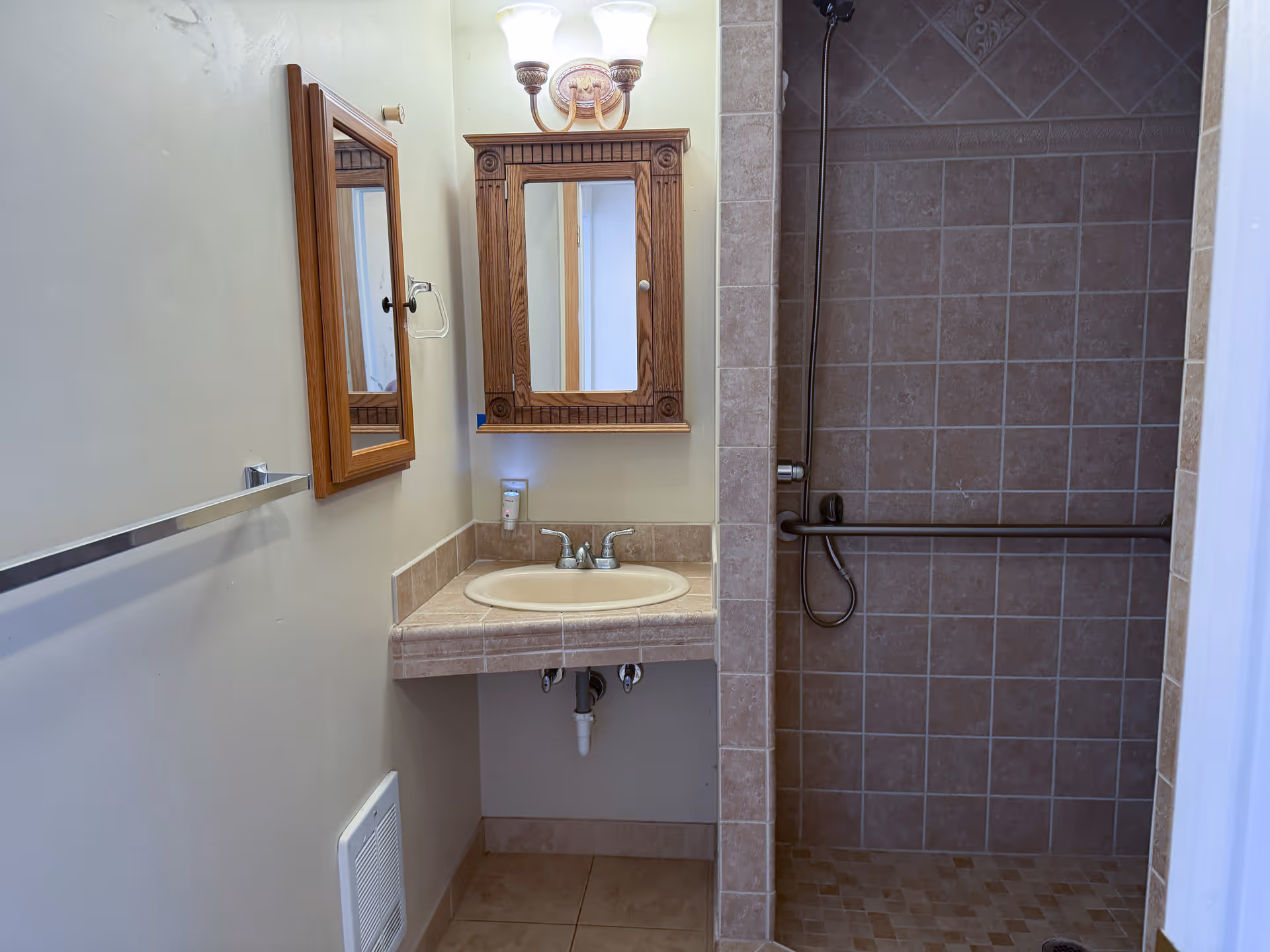 Bathroom with dual wooden-framed mirrors, sink, and tiled shower stall.
