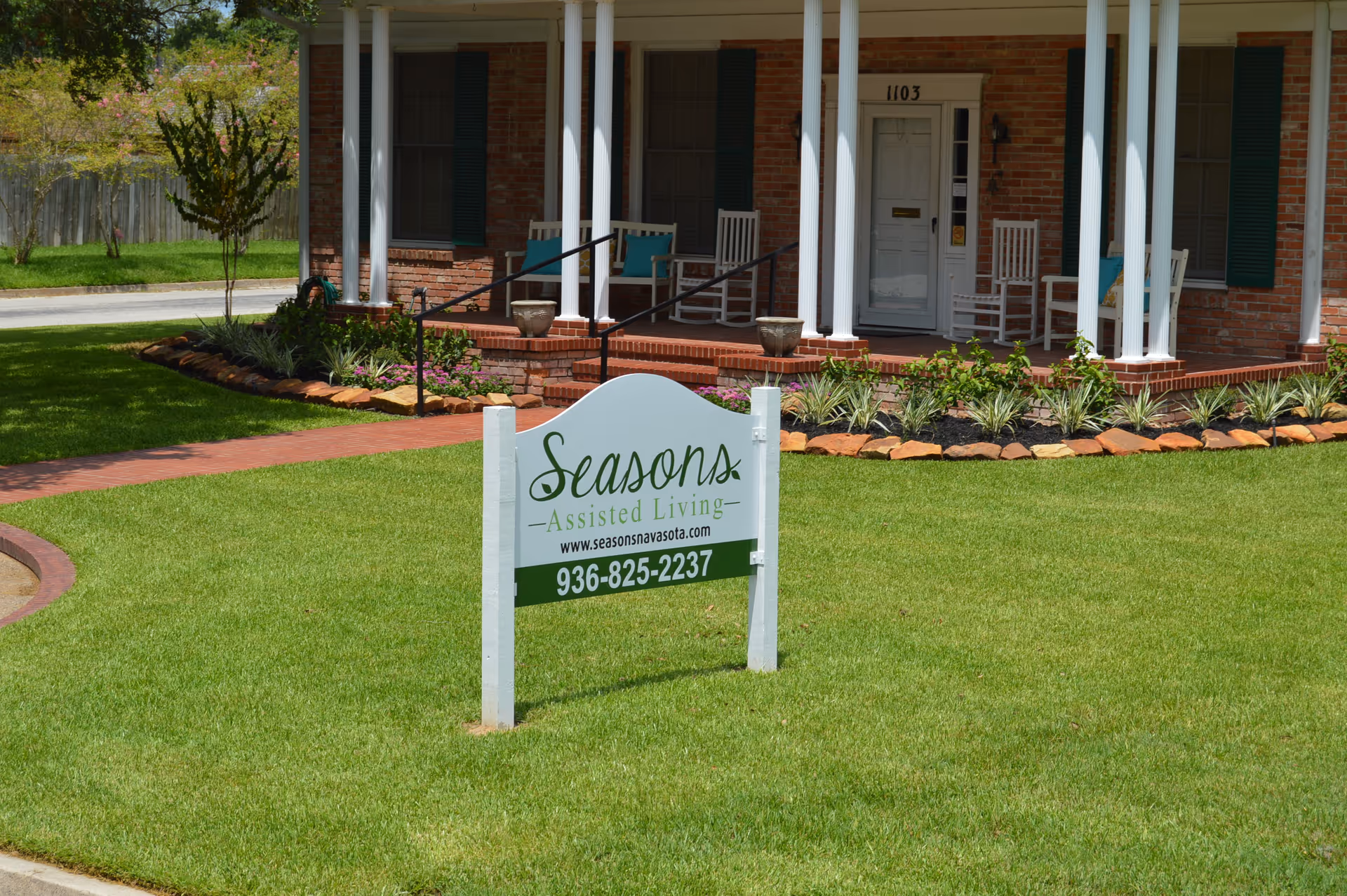 Front exterior of Seasons Assisted Living with porch seating and landscaped lawn.