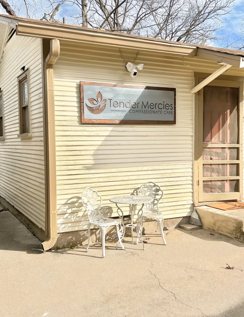 Beige exterior of Tender Mercies Compassionate Care with a small white metal outdoor seating set.