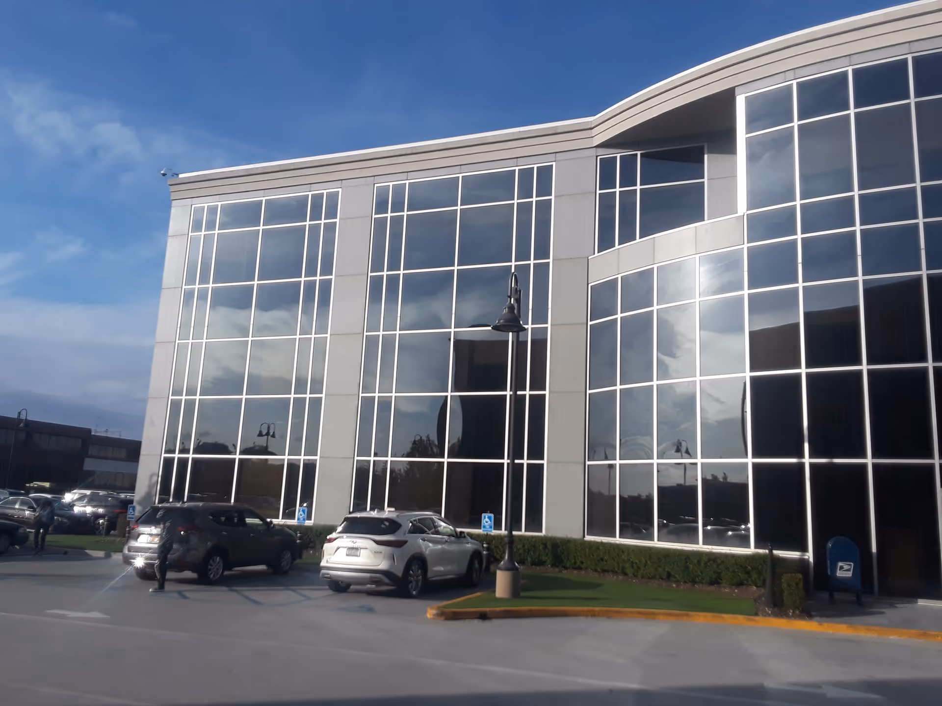 Modern glass-front medical building with a parking lot and blue sky above.