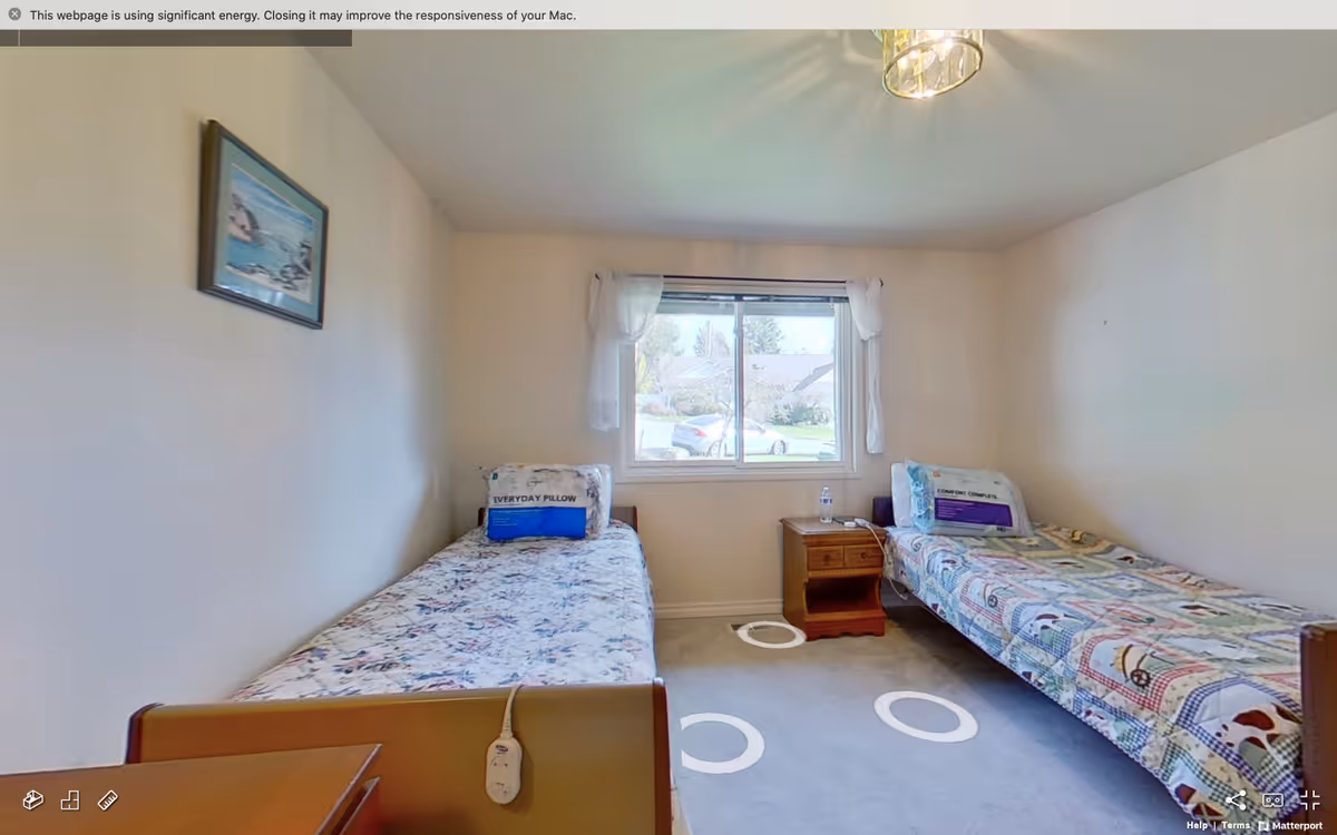 Two single beds in a small bedroom with a window, nightstand, and overhead light.
