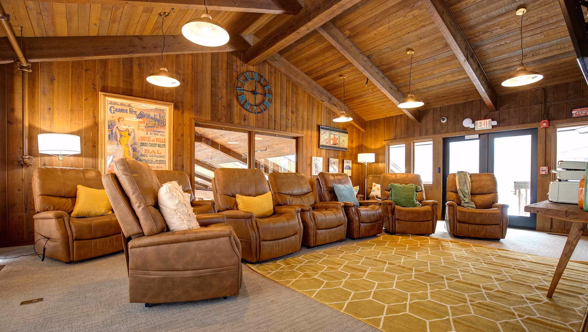 Cozy senior living lounge with brown leather recliners arranged on a patterned rug beneath a wooden beamed ceiling.