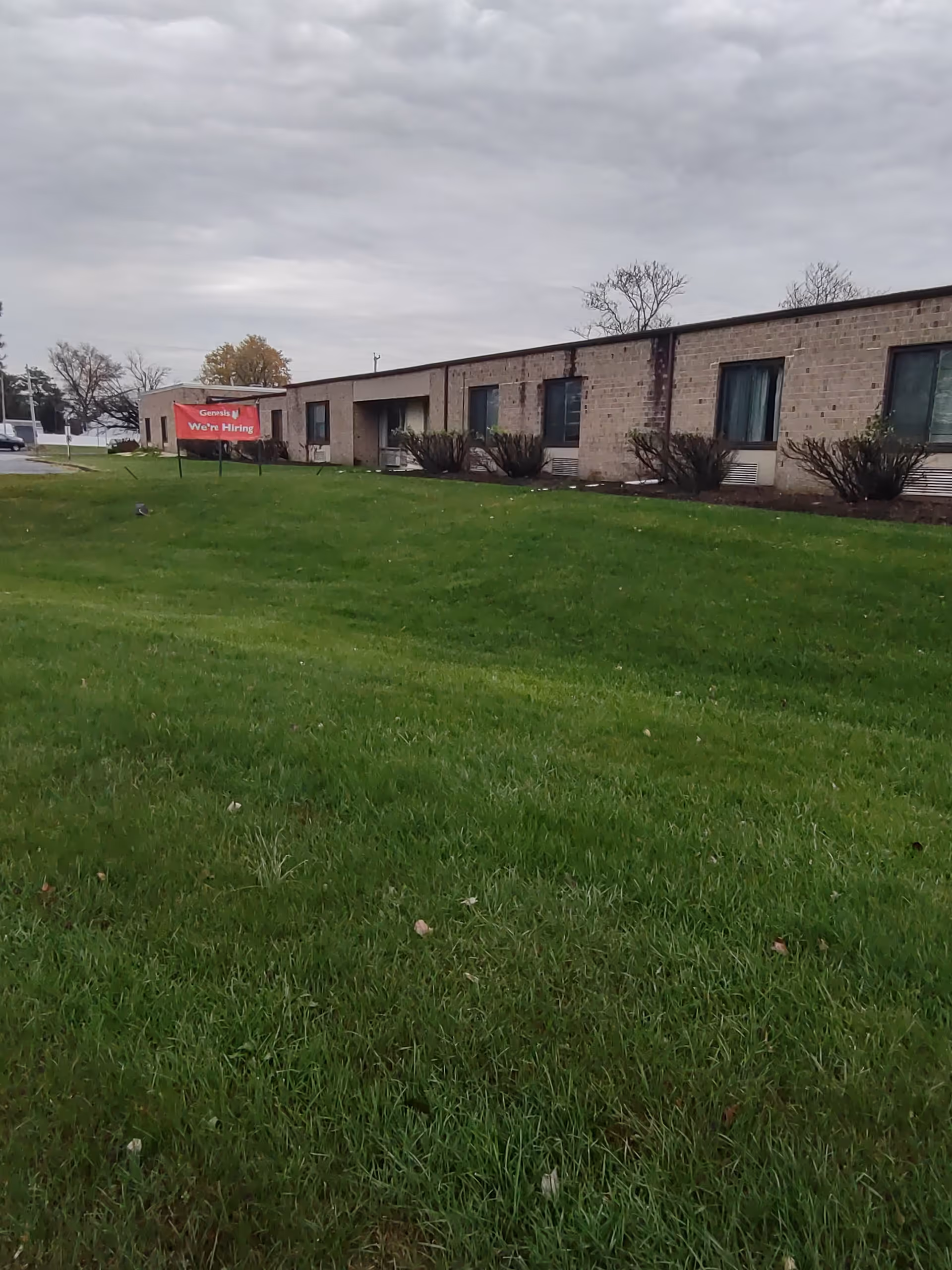 Exterior view of Hammonds Lane Center with green lawn and a We're Hiring sign