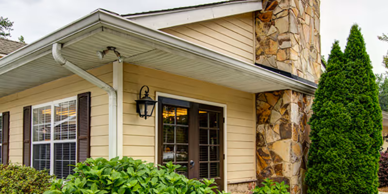 Exterior view of a beige senior living facility with stone veneer and greenery.