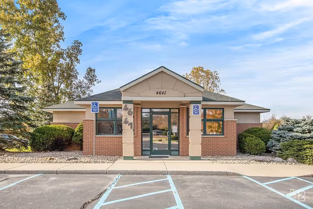 Front view of a brick senior living facility with glass entrance doors and accessible parking spaces.