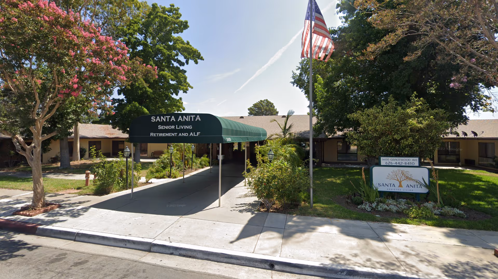 Front entrance of Santa Anita Senior Living with a green canopy, American flag, and a sign in a landscaped yard.