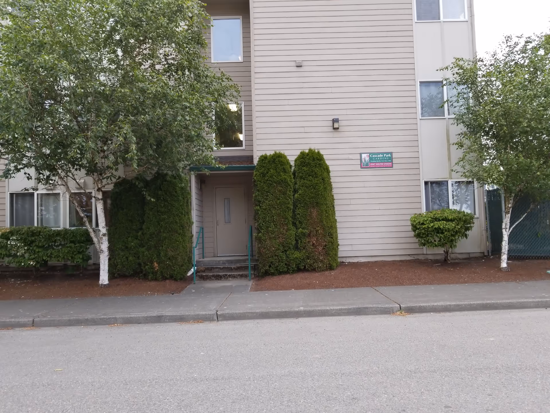 Front view of Cascade Park Gardens building with trees, shrubs, and a doorway entrance.