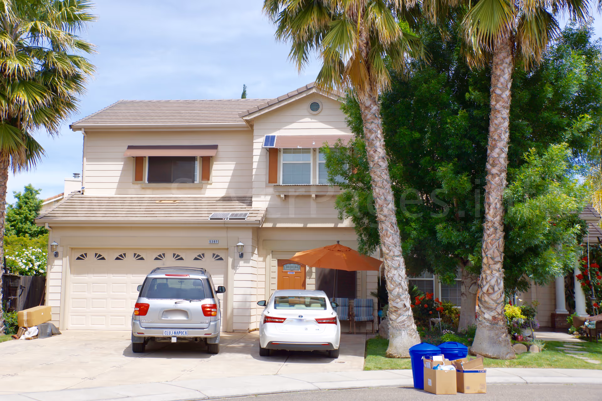 Two-story beige senior care home facade with cars and palm trees in front.