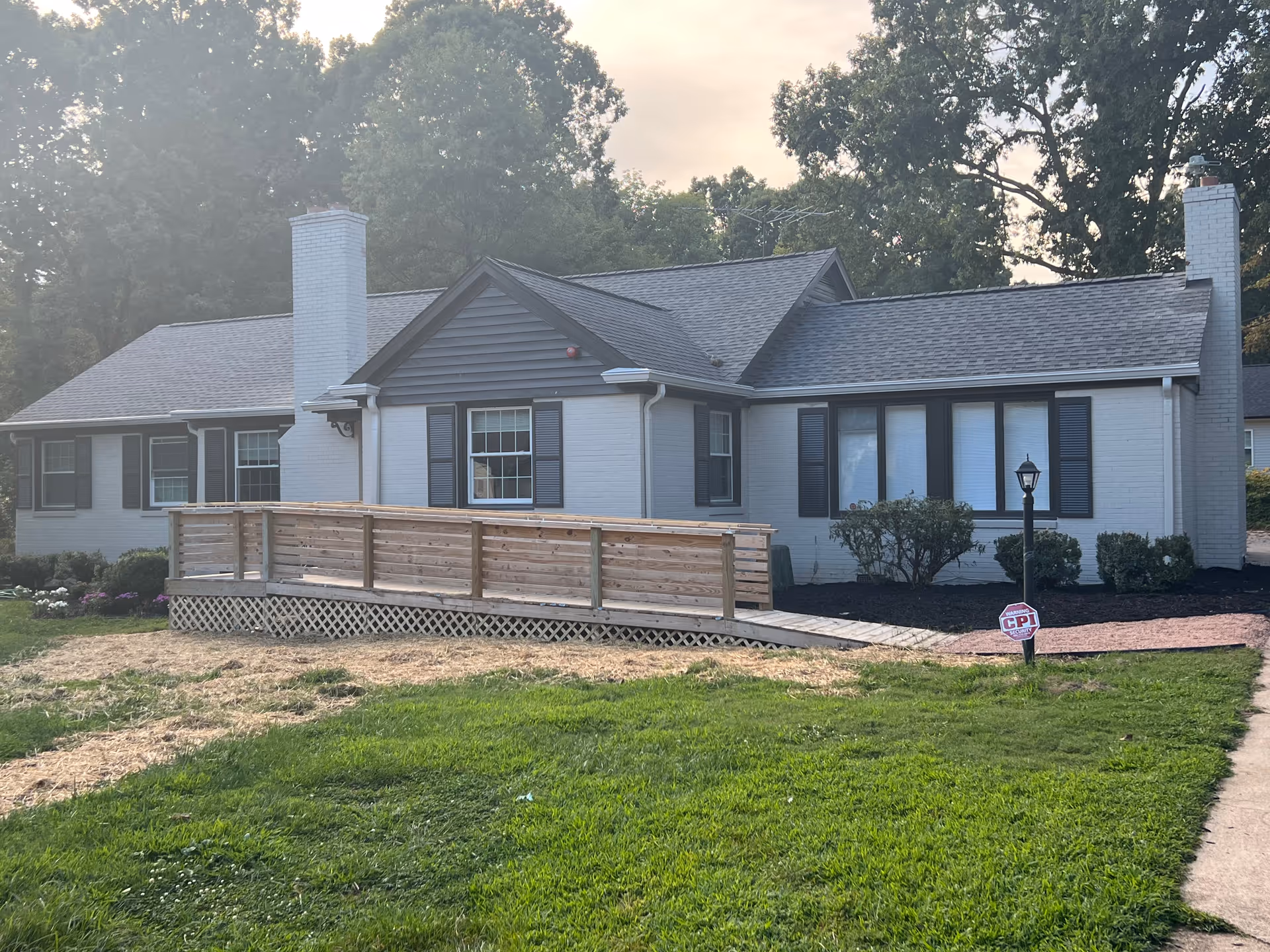 Single story white brick senior living facility with a wooden ramp and manicured lawn.
