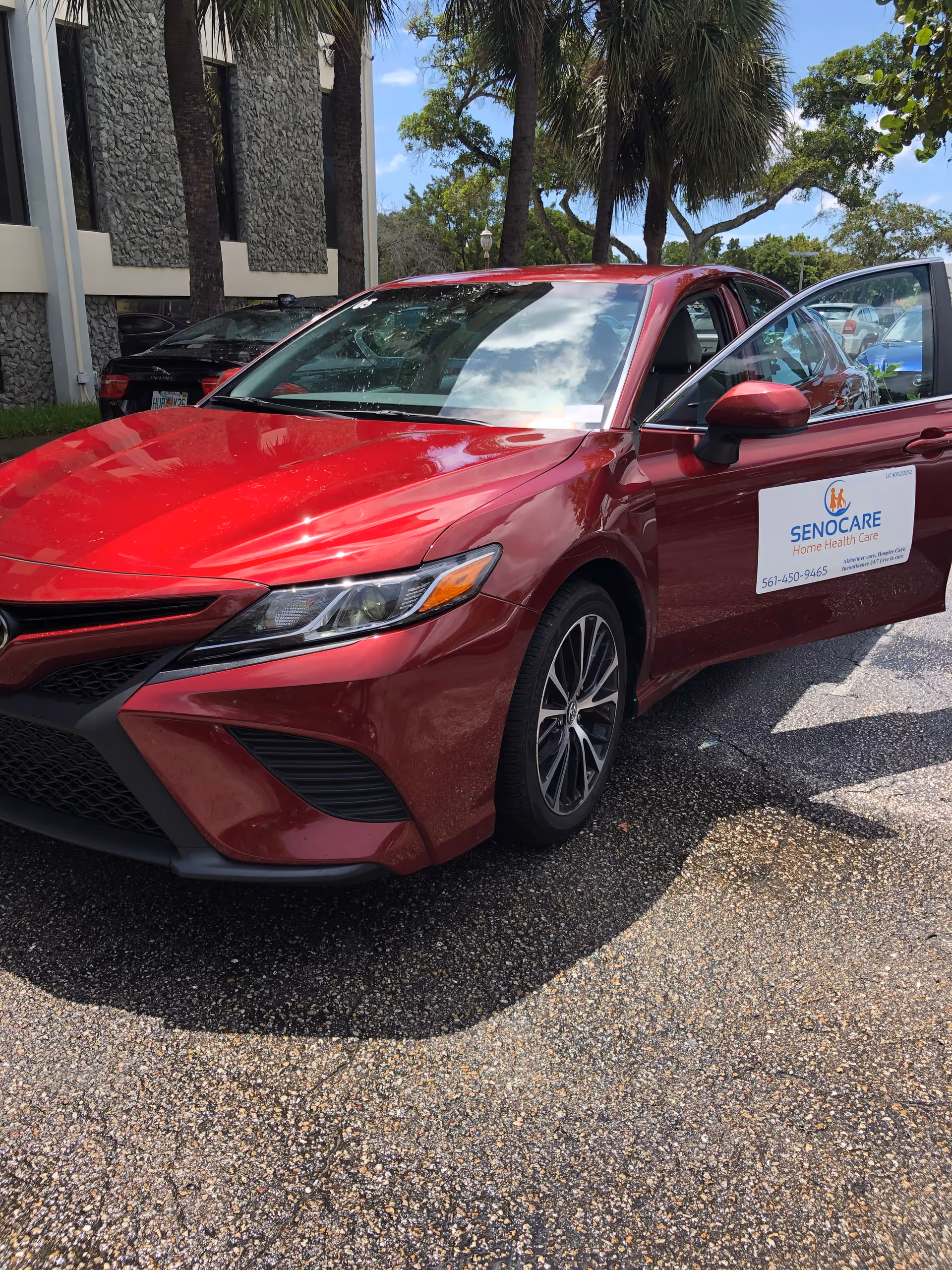 Red Senocare-branded car parked outside a facility with palm trees visible.