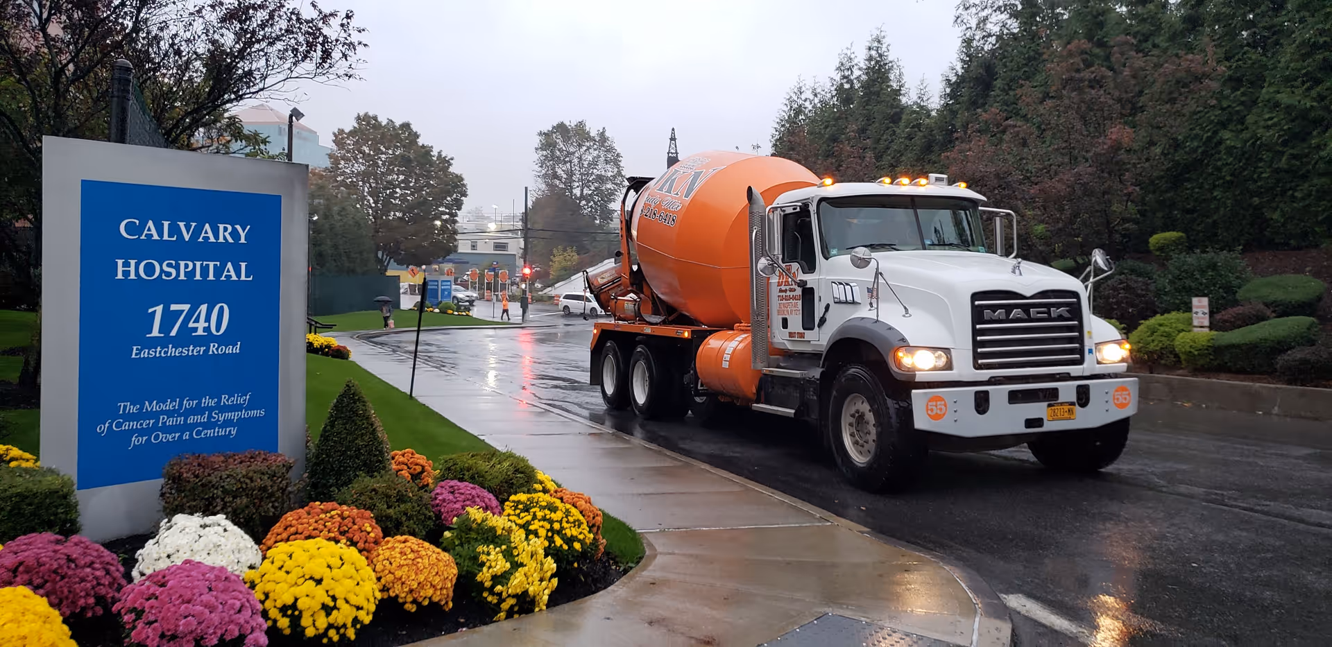 A concrete mixer truck drives past the Calvary Hospital entrance on a wet road.