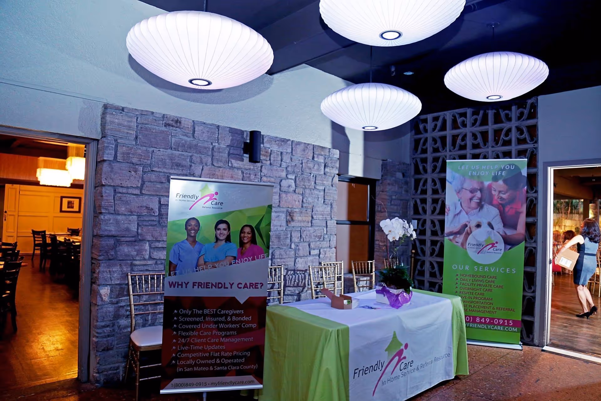 Indoor reception area featuring Friendly Care banners, a table, and round white ceiling lamps.