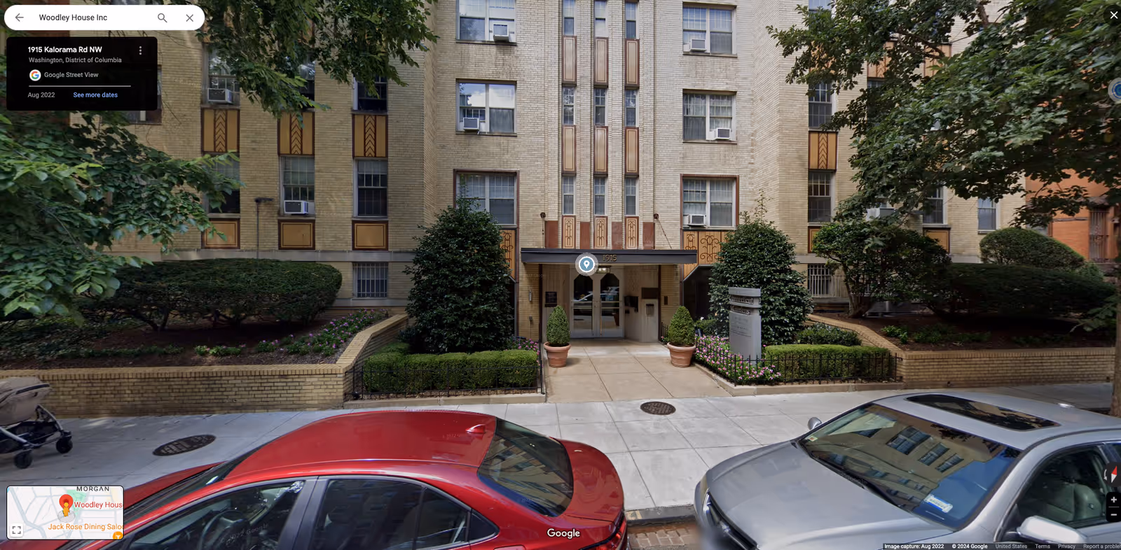 Exterior view of Woodley House Inc entrance with greenery and parked cars along the street.