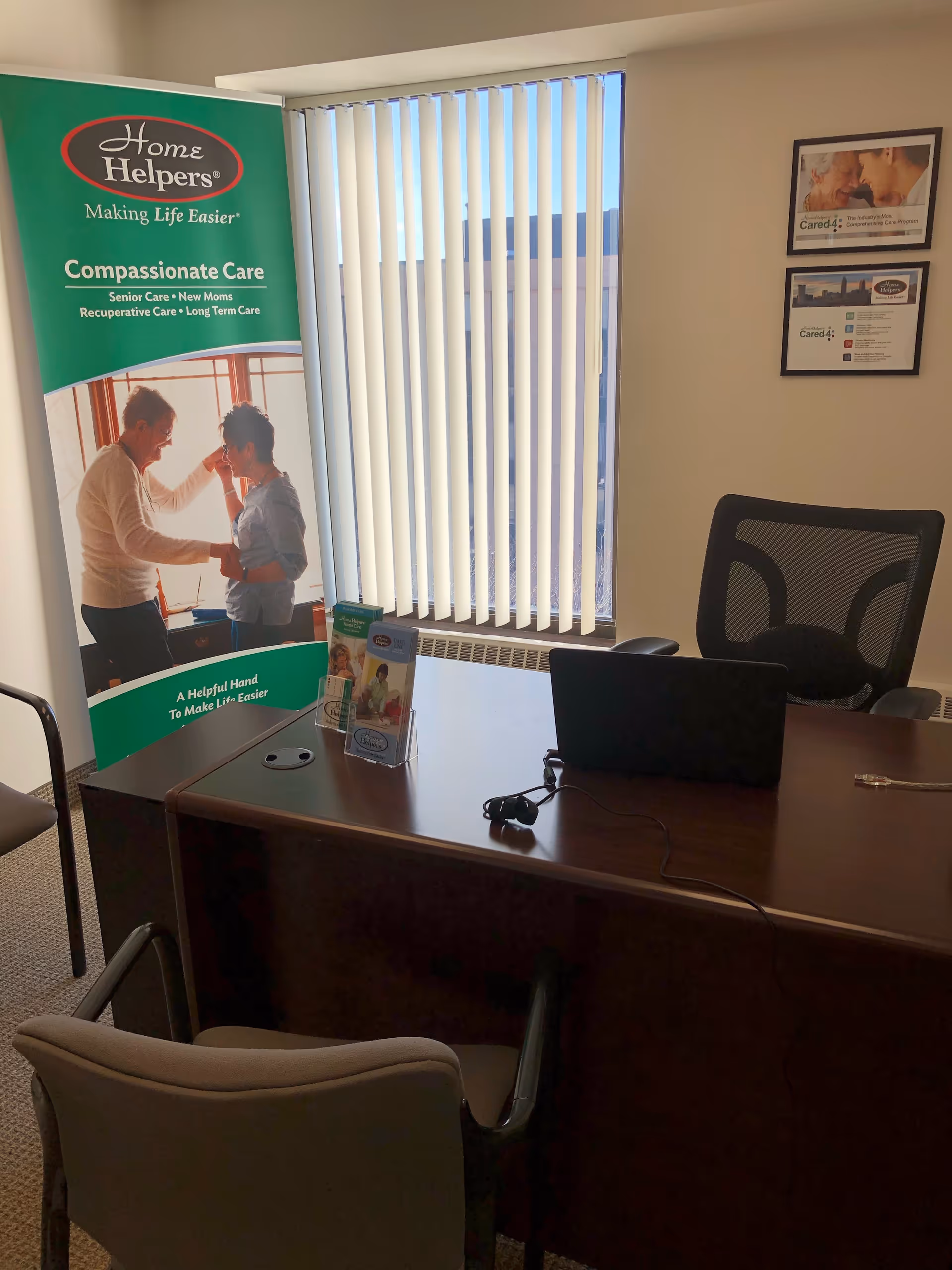 Office reception area with a Home Helpers banner, desk, laptop, and blinds.