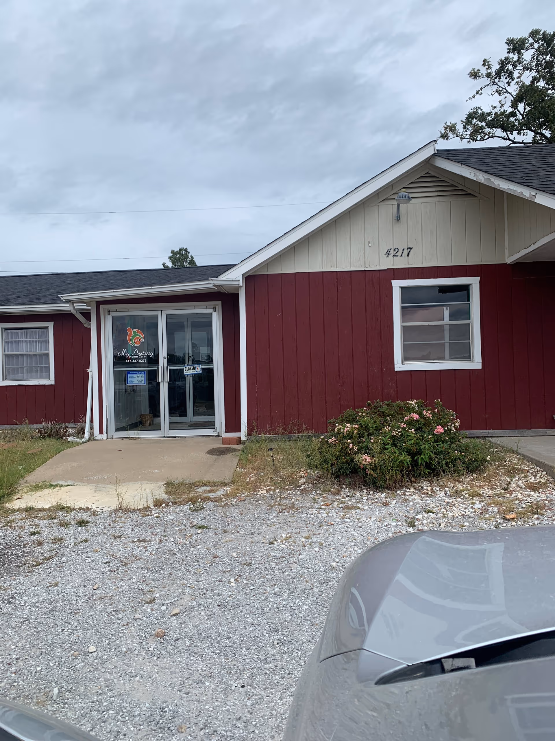 Red exterior building with a glass front door and gravel parking area.