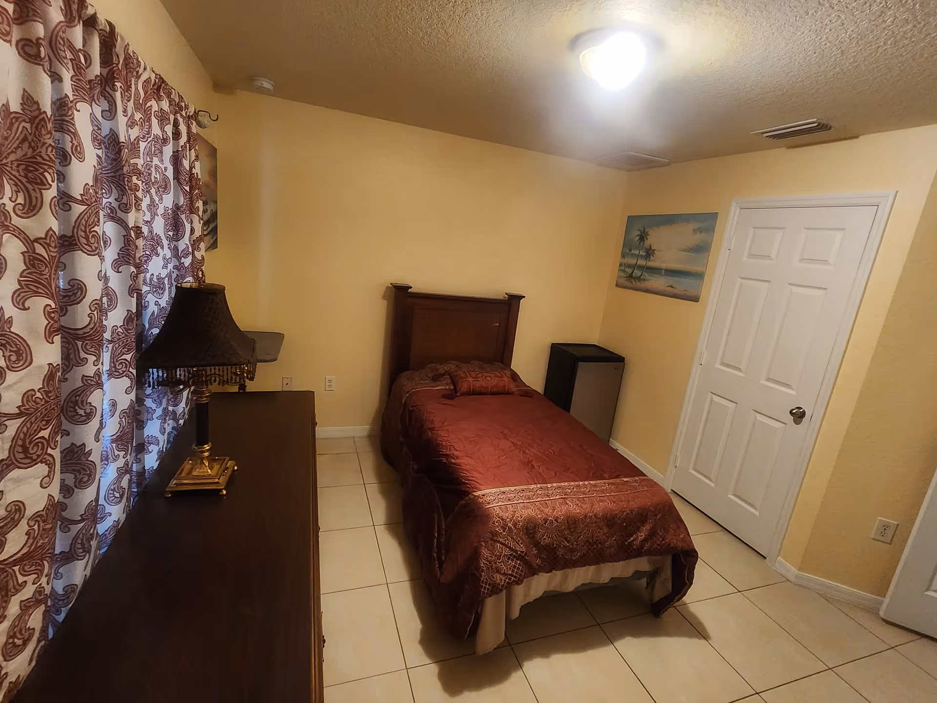 Small bedroom with a single bed, dresser, lamp, and patterned curtains.