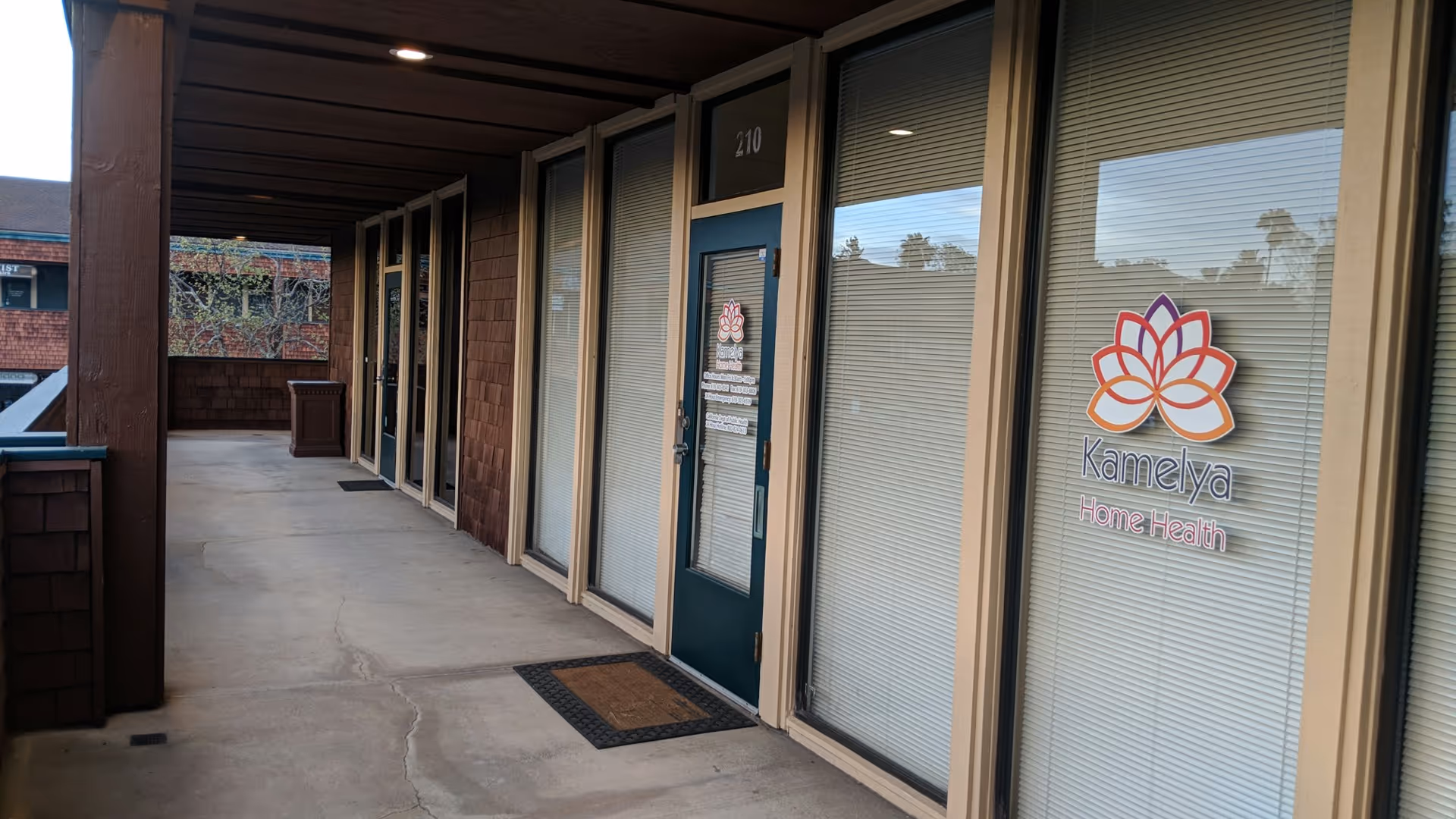 Exterior walkway along Kamelya Home Health with glass doors and logo.