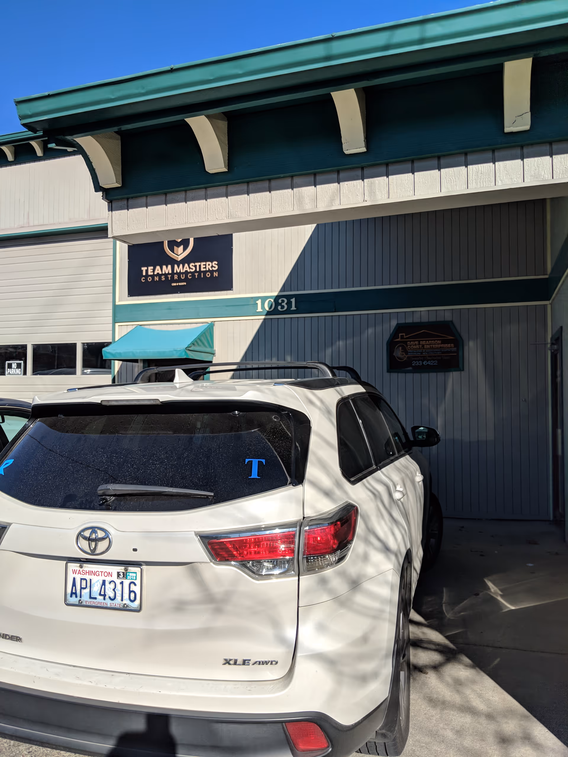 White Toyota SUV parked outside teal-trimmed building with Team Masters Construction sign.