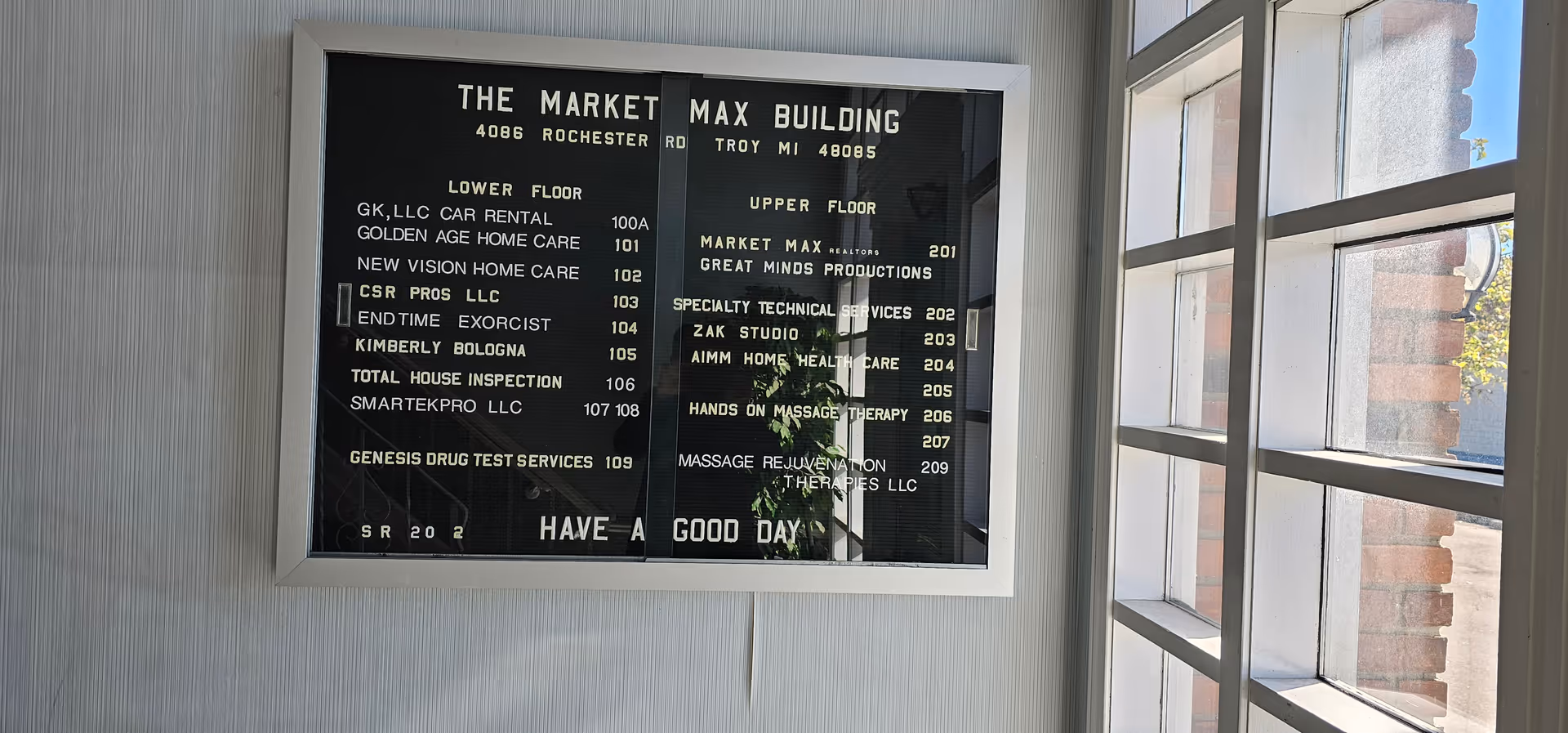 Indoor wall directory signboard listing offices on multiple floors beside a window.