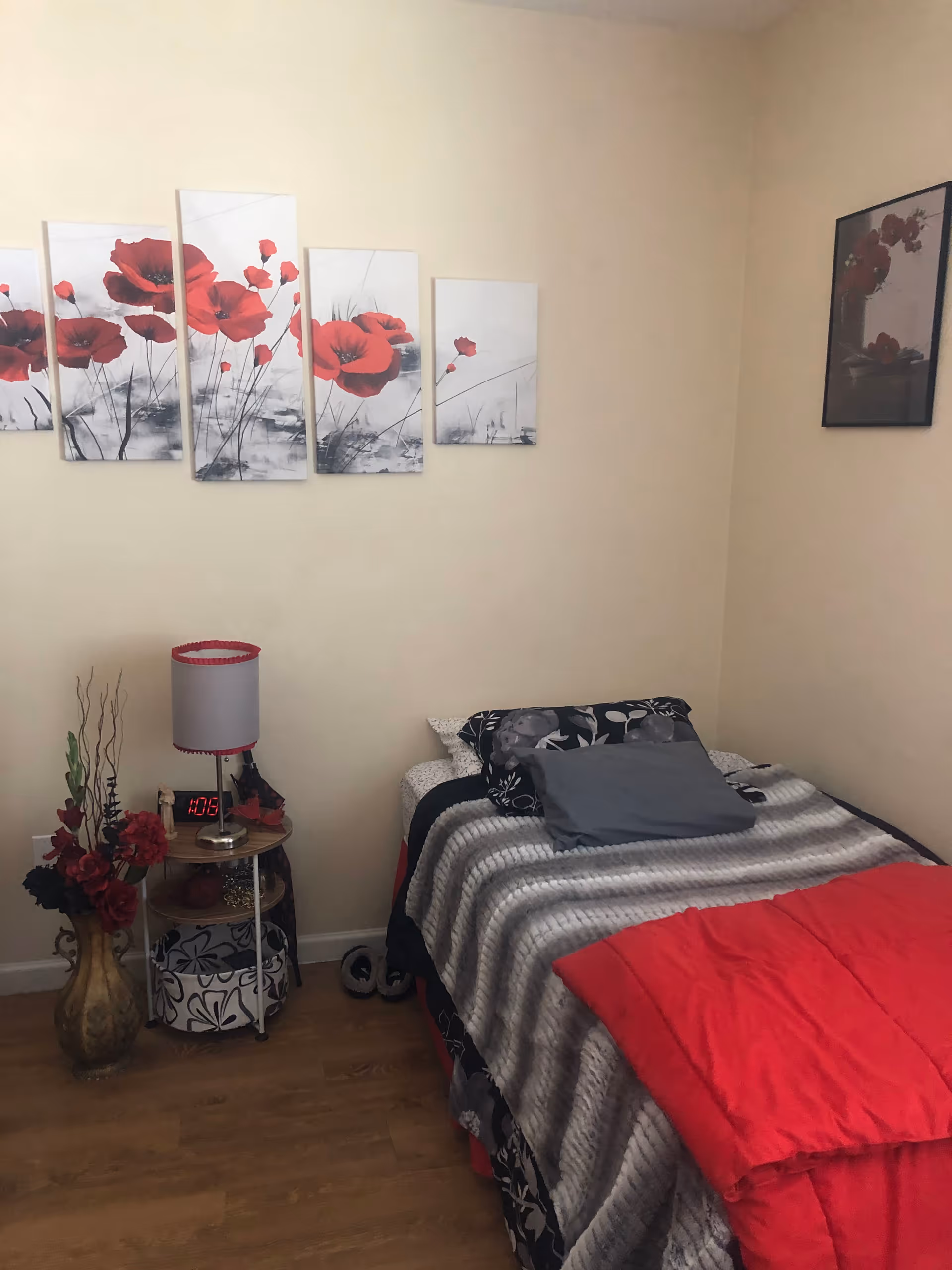 Cozy bedroom with a twin bed, red comforter, lamp, and wall art.